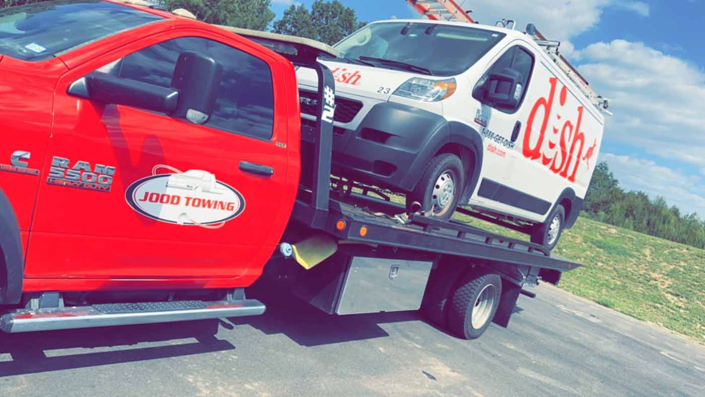 A red truck is towing a white van on a flatbed tow truck.