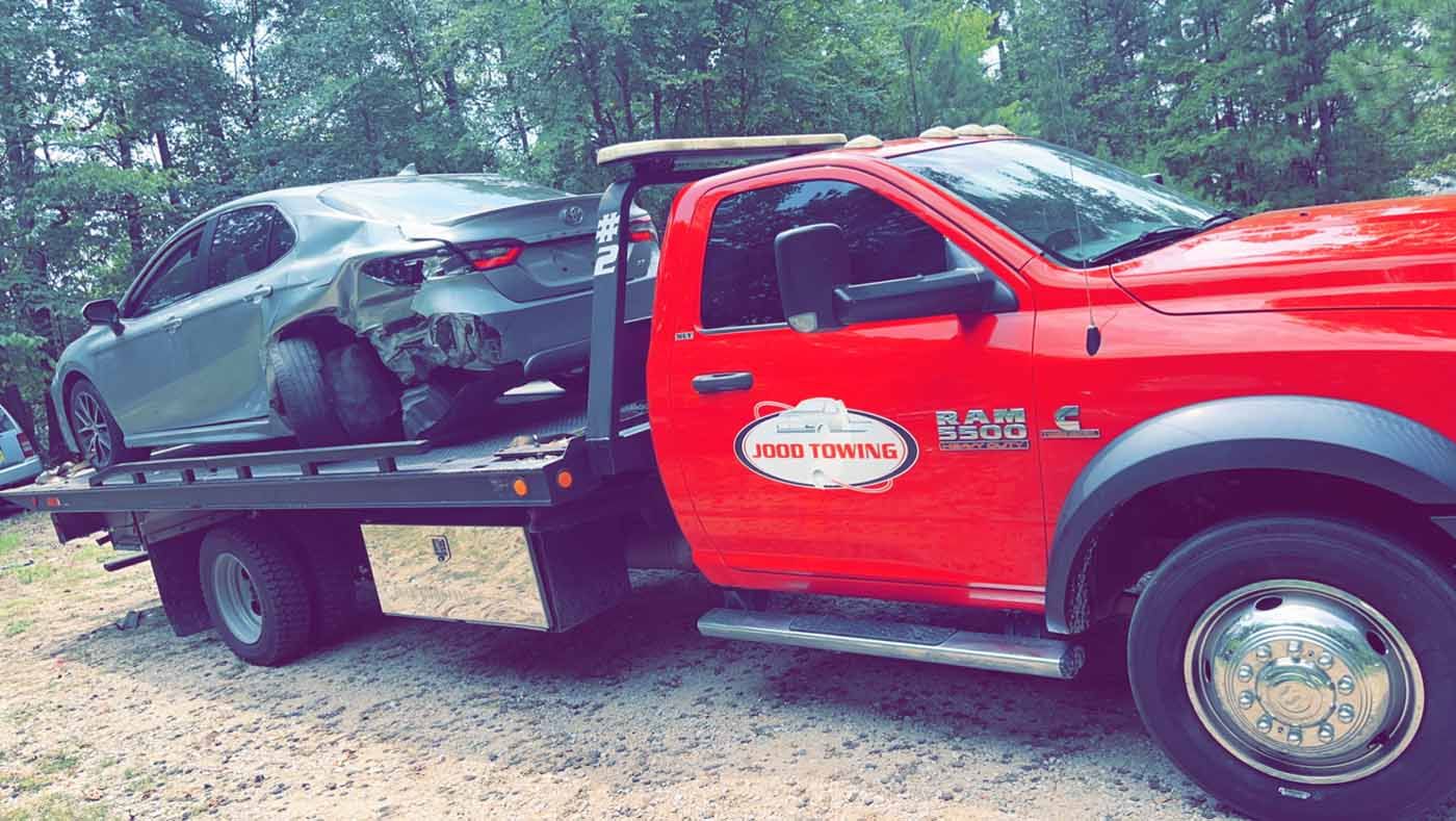 A red tow truck is towing a damaged car.