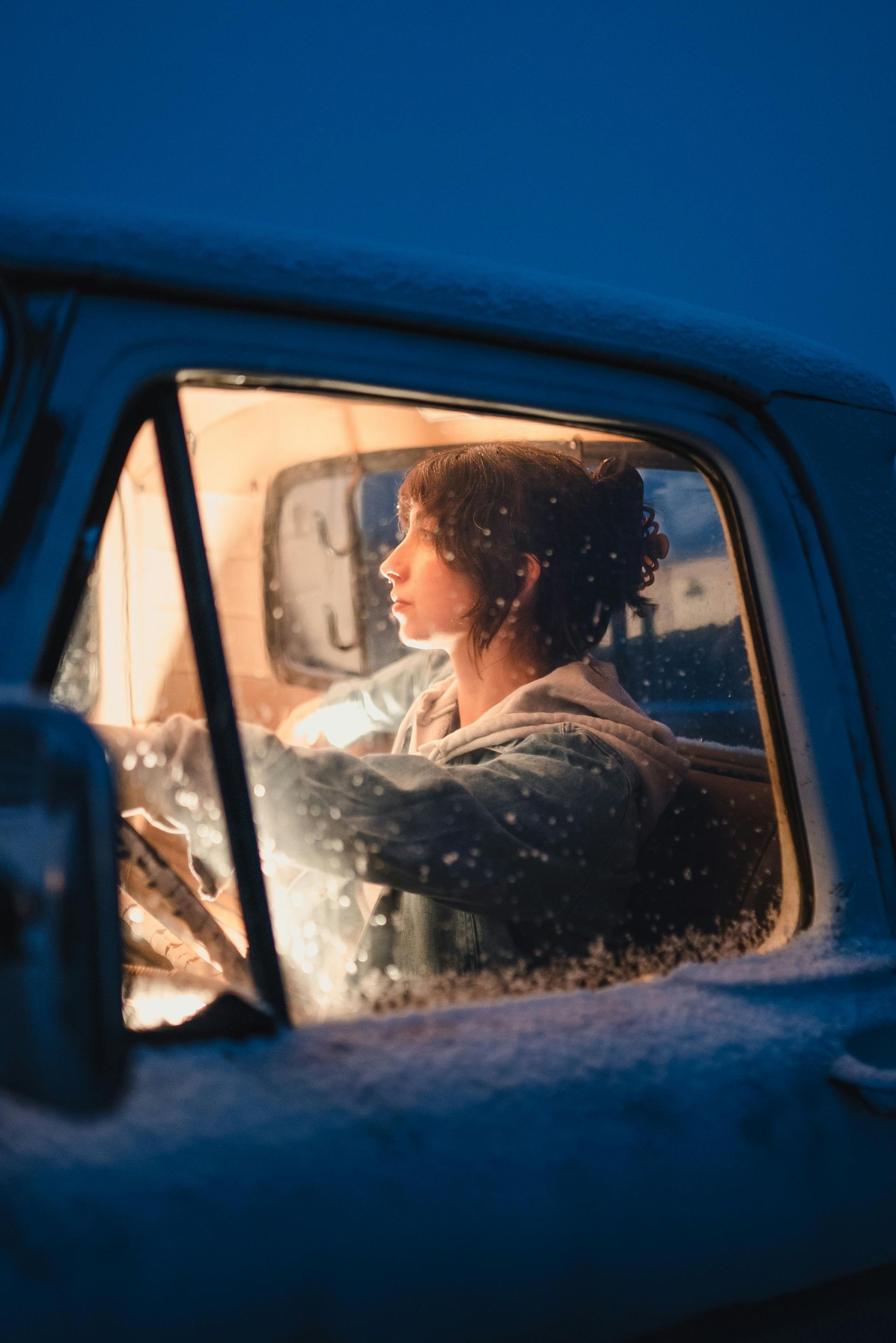 A woman is driving a truck in the snow at night.