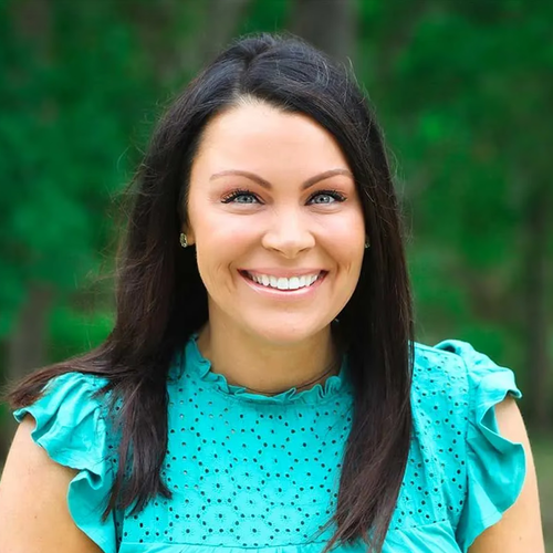 A smiling person with long dark hair wearing a bright teal, eyelet-patterned ruffled top against a soft green background.