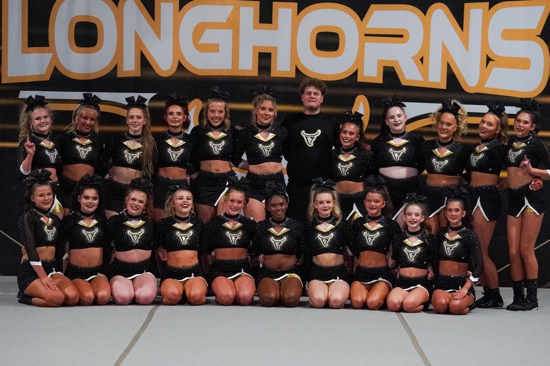 Cheerleading team in black uniforms poses on a patterned carpet.