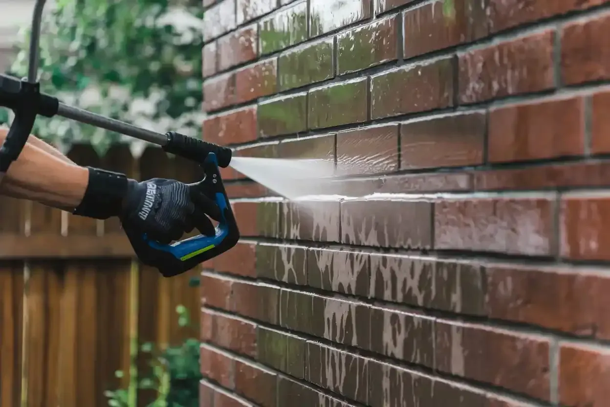 A person is cleaning a brick wall with a high pressure washer.