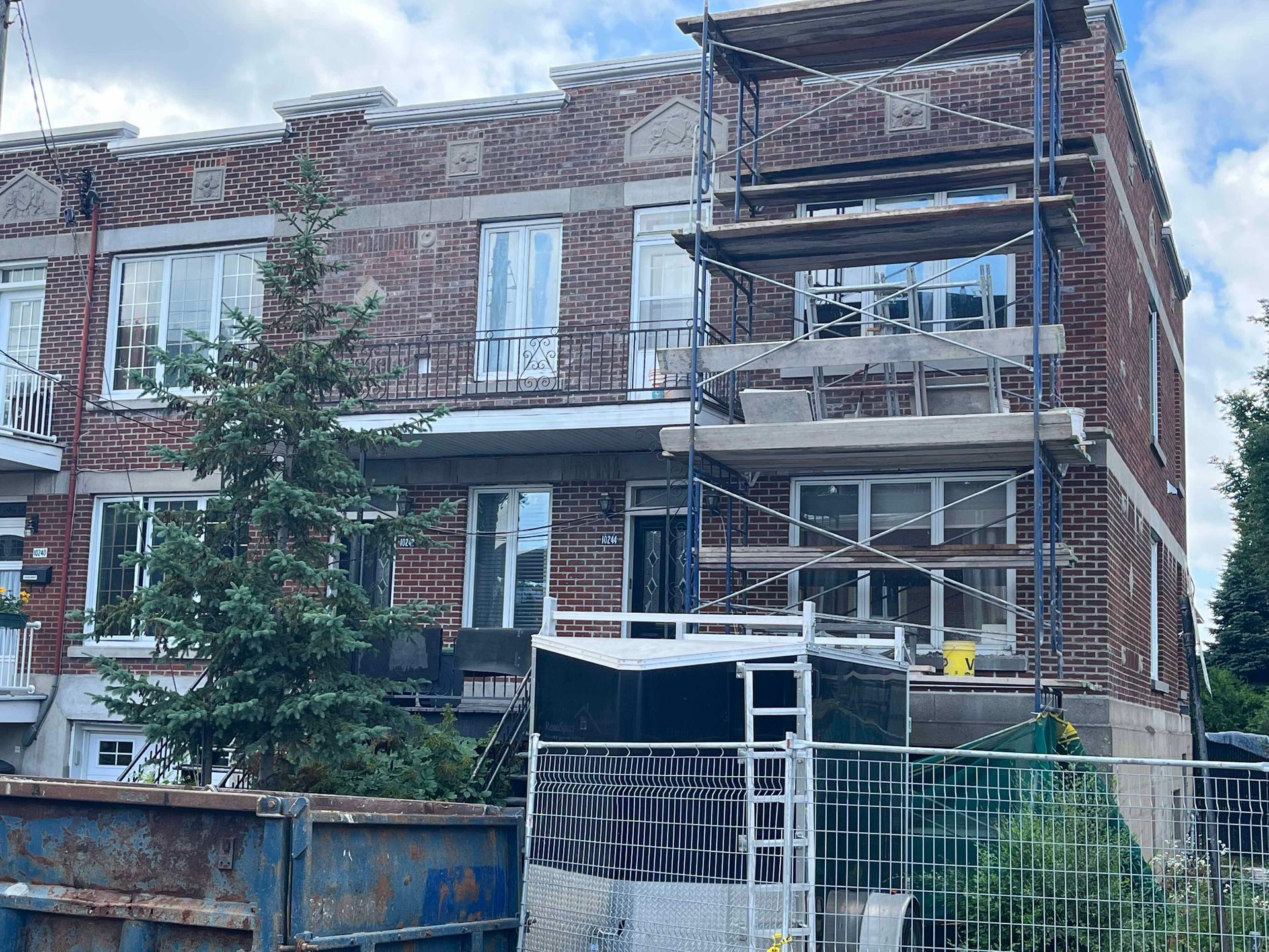 Un grand bâtiment en briques en construction avec un échafaudage et une benne à ordures devant.