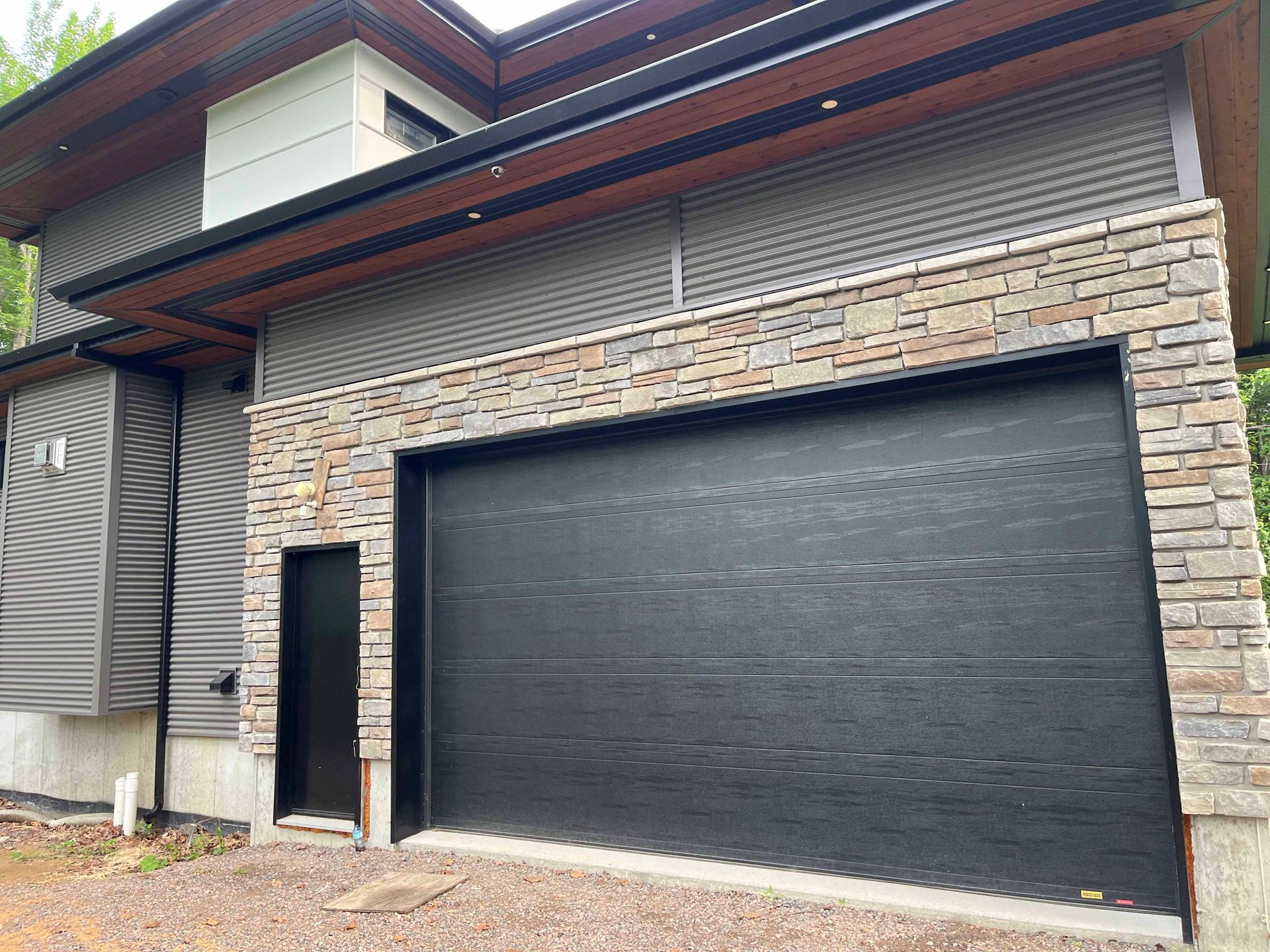 Une grande maison avec une porte de garage noire et un mur en pierre.