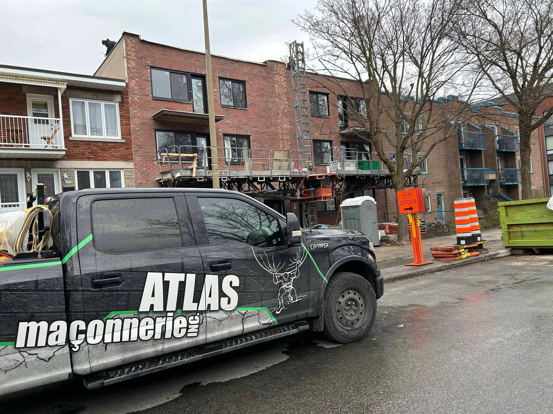 Un camion noir est garé sur le bord de la route devant un bâtiment en briques.