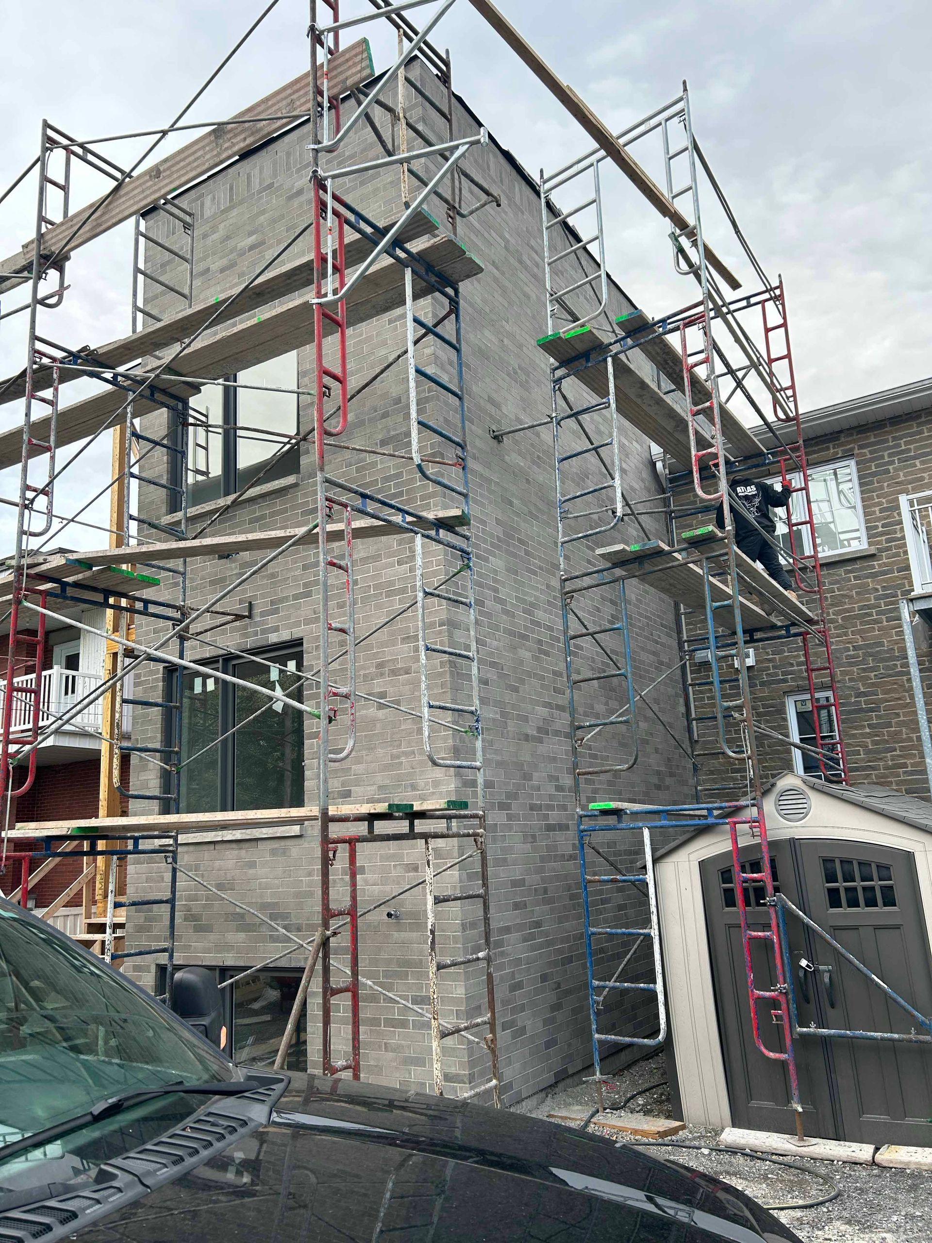 Un bâtiment en construction avec des échafaudages autour et une voiture garée devant.