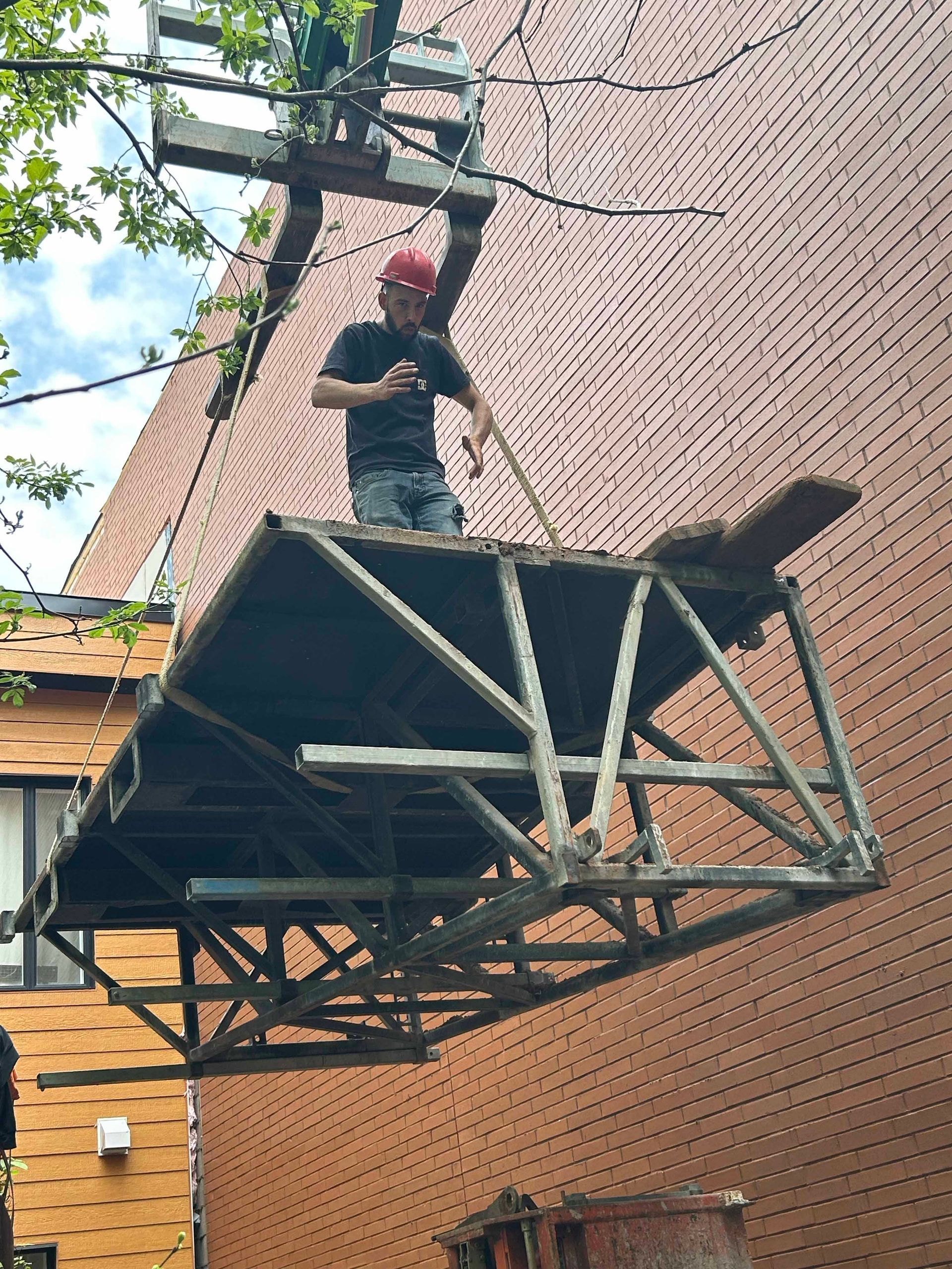 Un homme se tient debout au sommet d'une structure métallique soulevée par une grue.