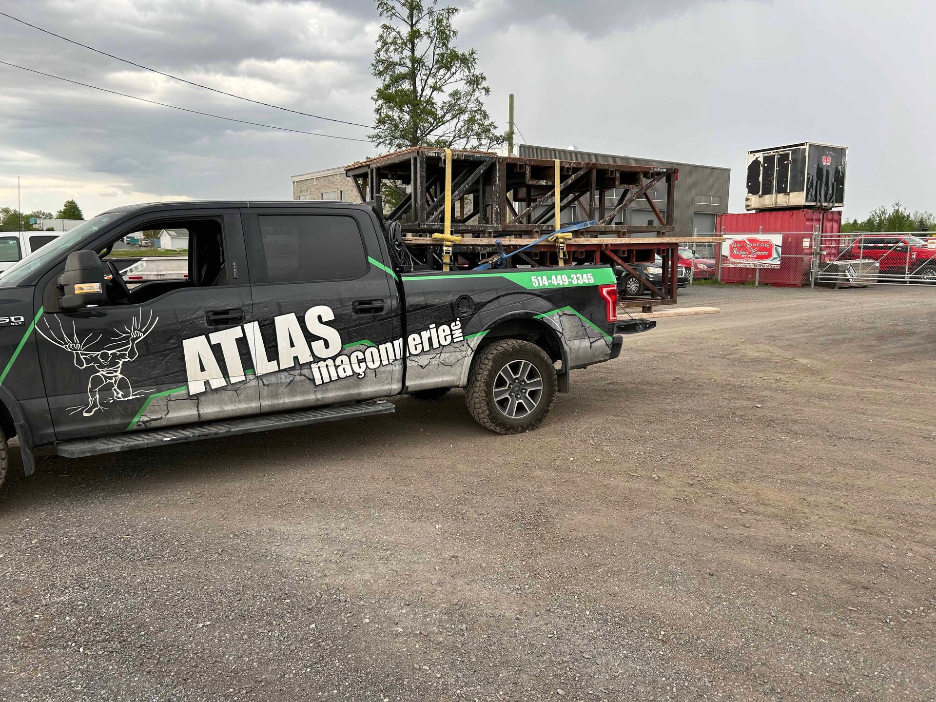 Une dépanneuse Atlas noire est garée sur un terrain en gravier.