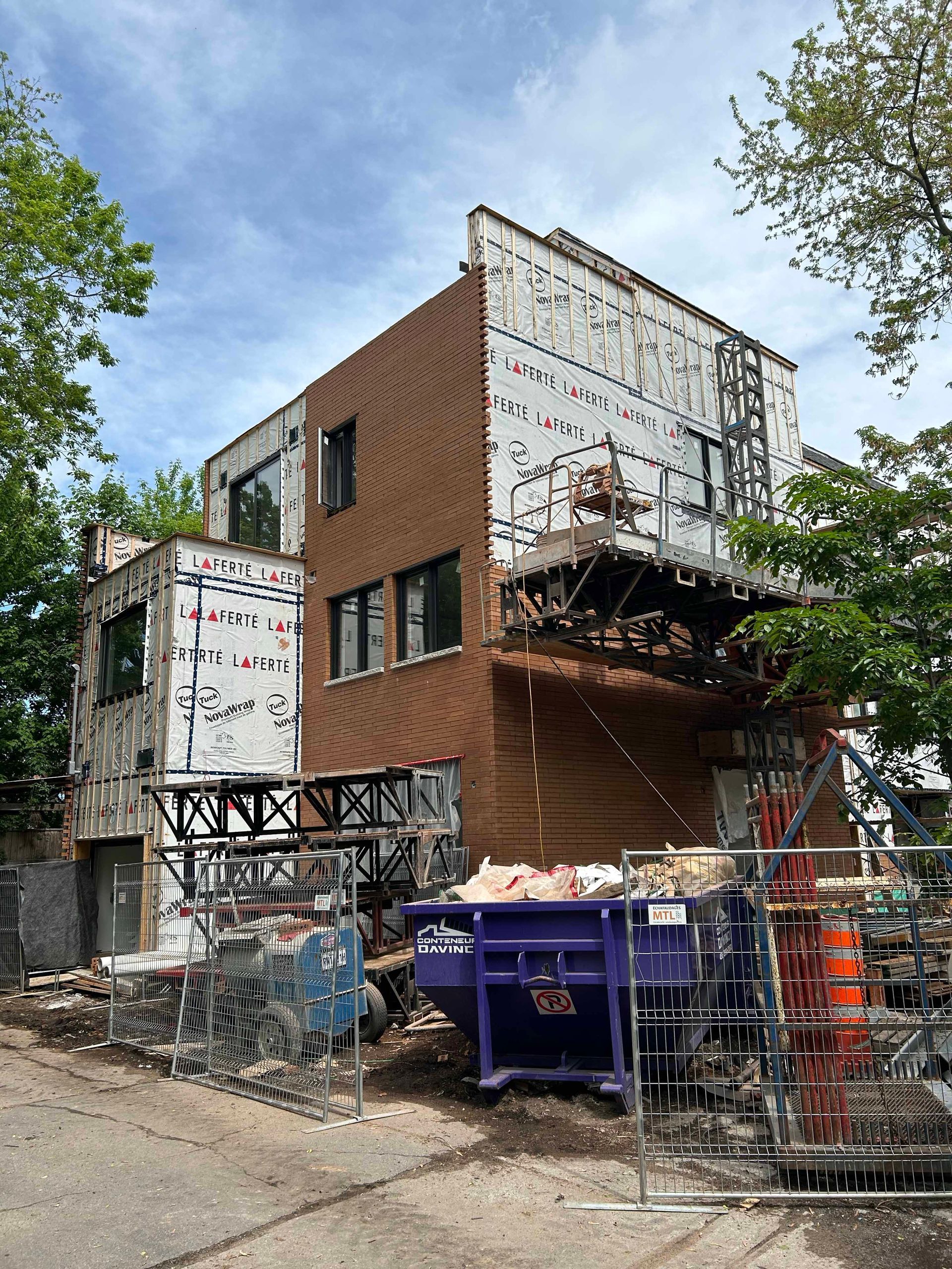 Un bâtiment en construction avec une benne violette devant.