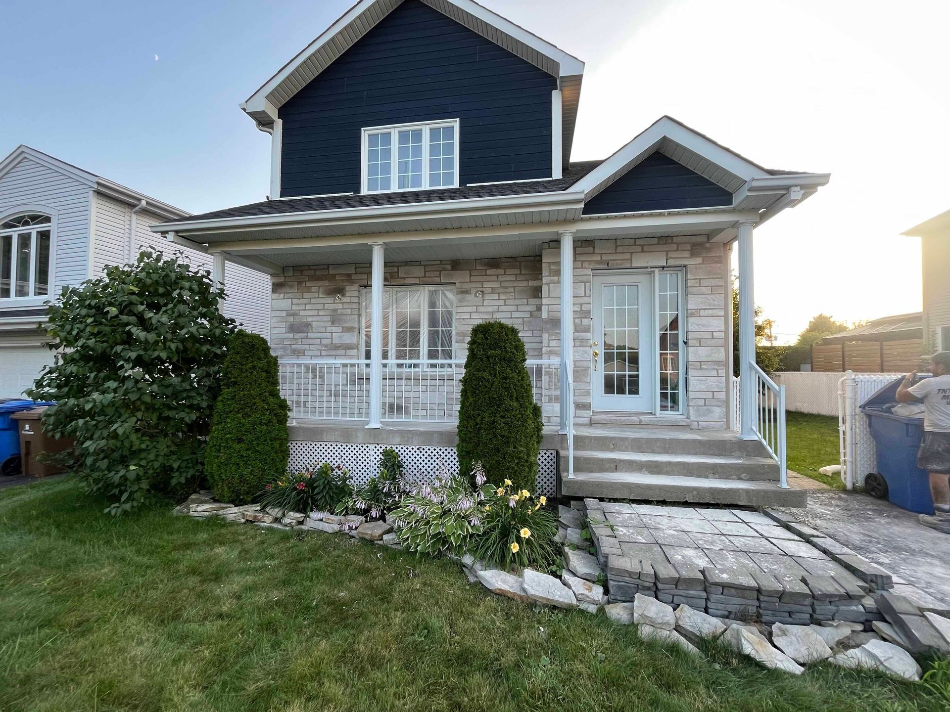 Une maison avec un revêtement bleu et un porche blanc est située au sommet d'une pelouse verte luxuriante.