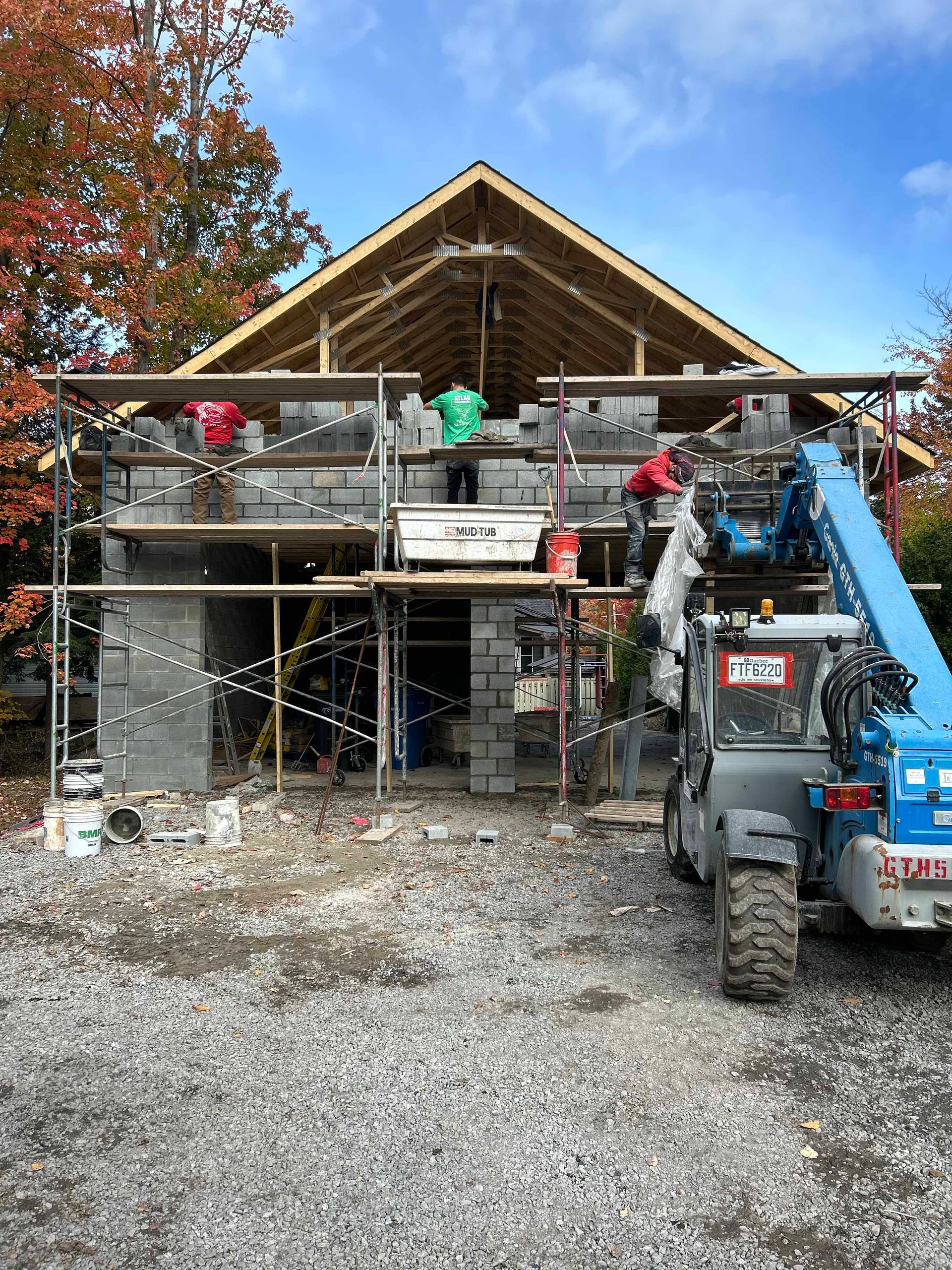 Une maison est en construction avec un échafaudage et un chariot élévateur devant.