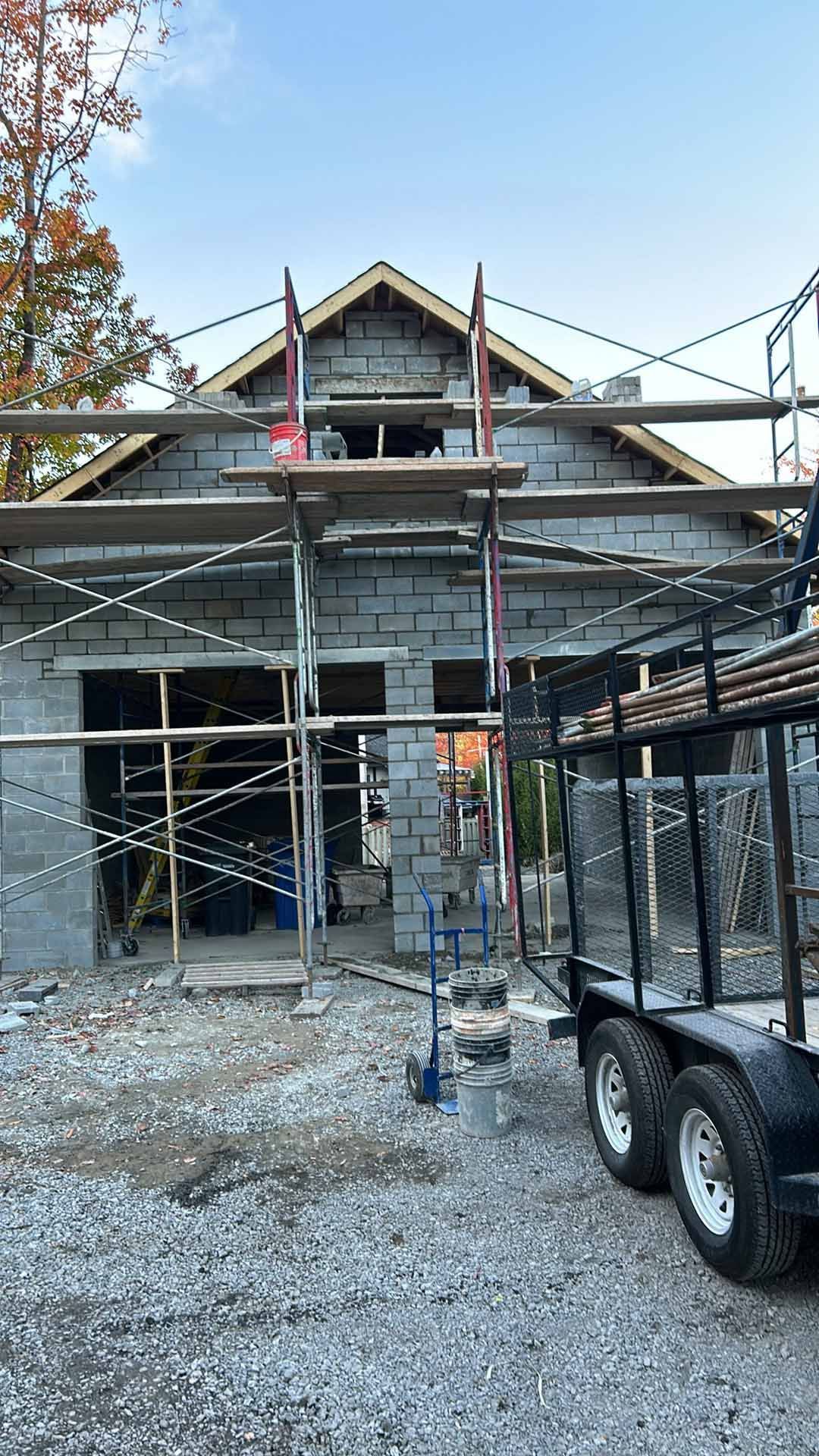 Une maison est en construction avec un échafaudage et une remorque garée devant.