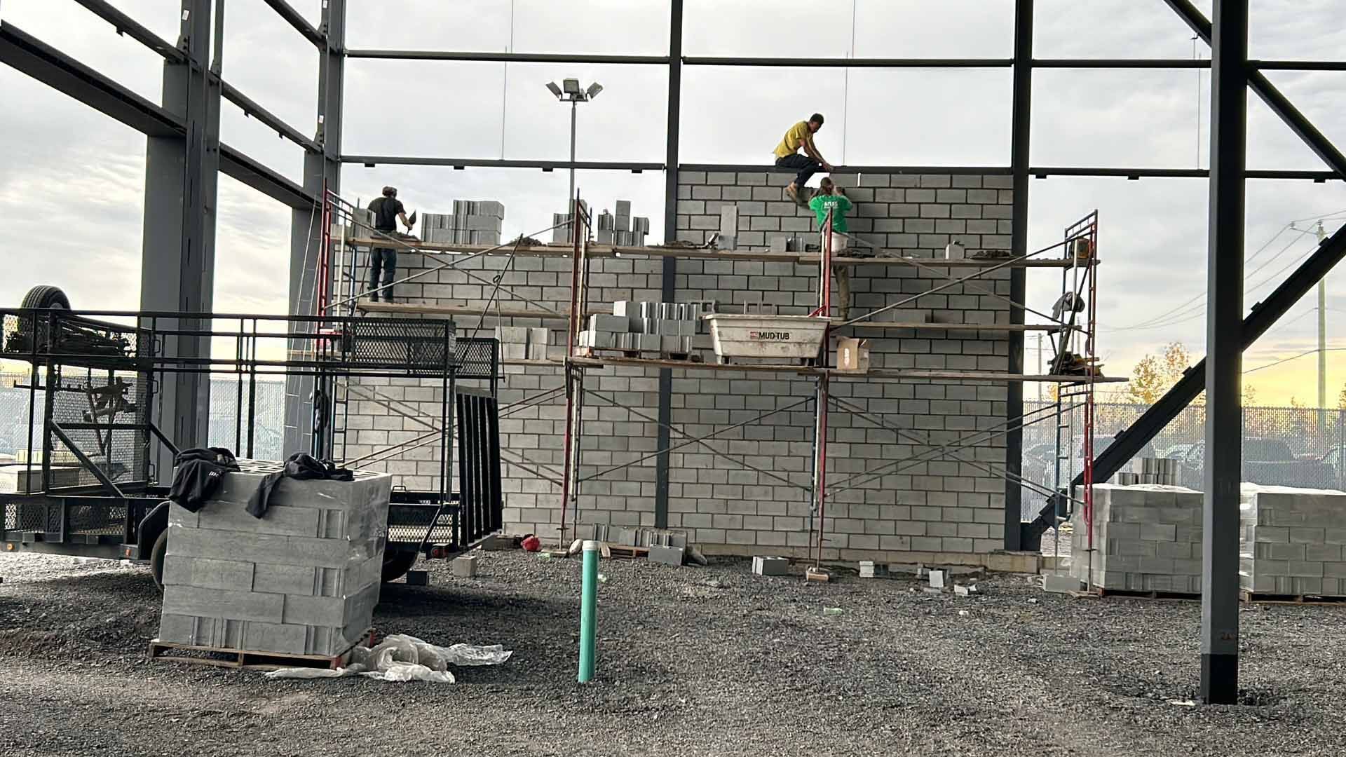 Un groupe d'ouvriers du bâtiment travaille sur un grand mur de briques.