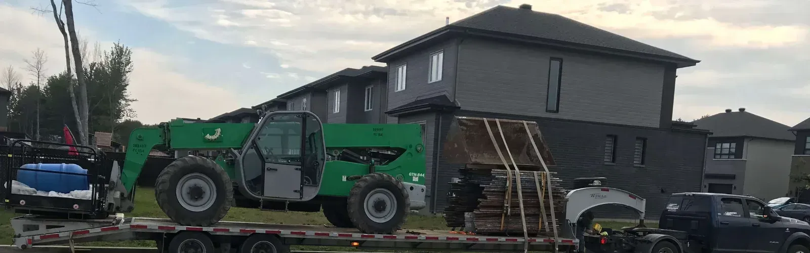 Un chariot élévateur vert est assis sur une remorque devant une maison.