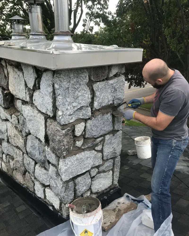 Un homme travaille sur une cheminée en pierre.