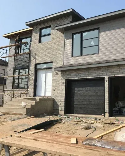 Une grande maison en briques avec une porte de garage noire est en cours de construction.