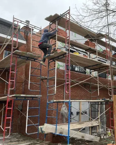 Un homme grimpe sur un échafaudage au sommet d'un bâtiment en briques.