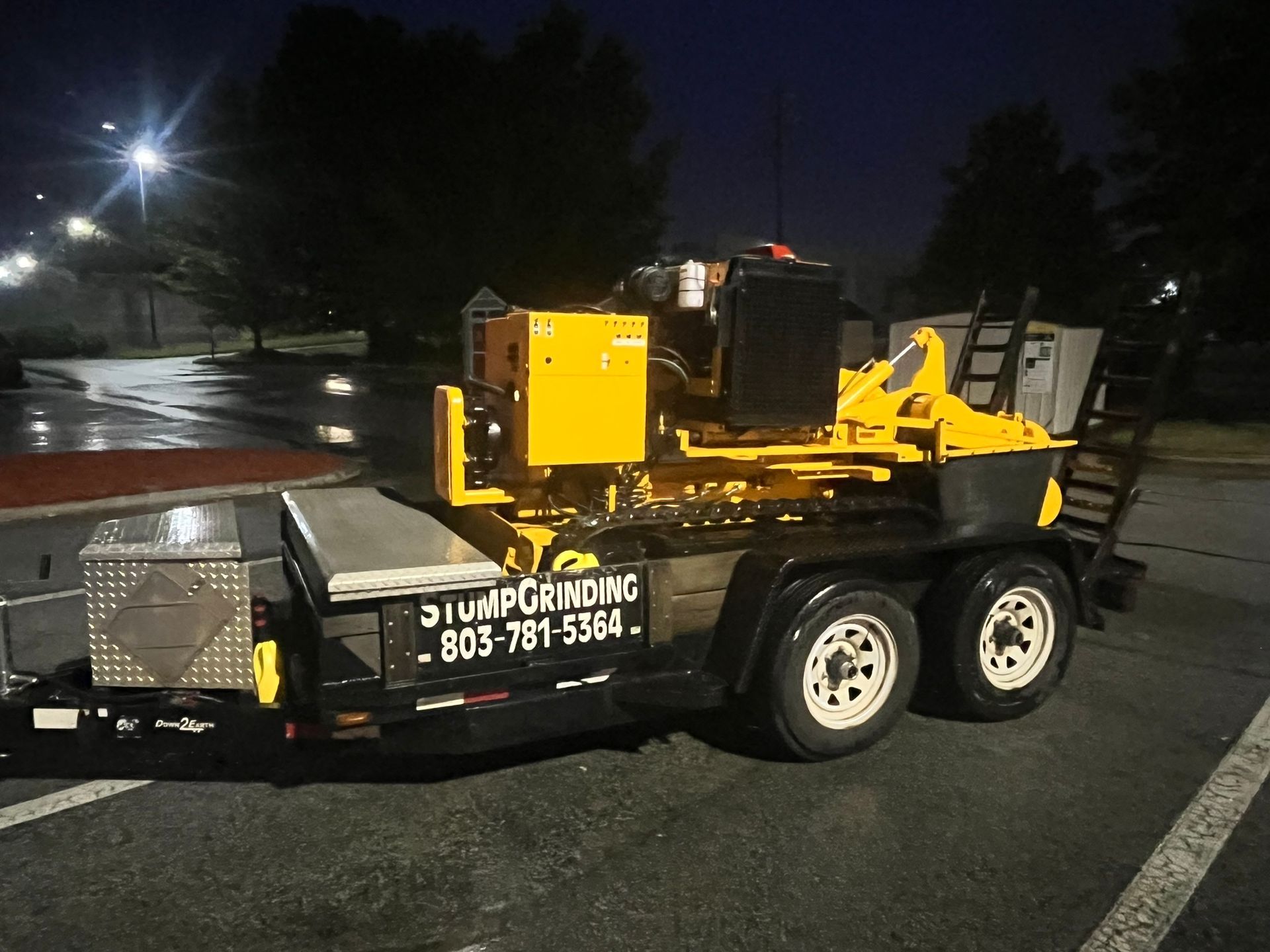 A yellow tractor is cutting a tree stump in the ground.