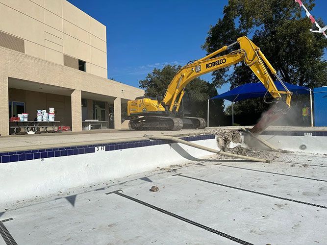 A bulldozer is cleaning a swimming pool in a backyard.