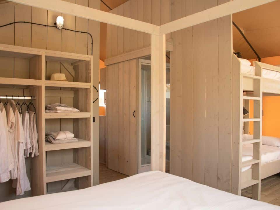 Modern hotel room interior featuring a wooden closet with white clothing and a set of bunk beds.