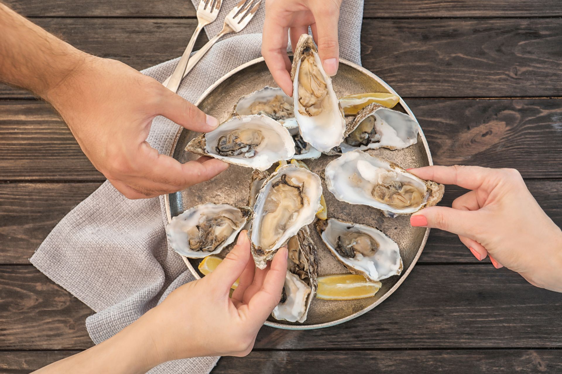 Hands reaching for oysters on a plate, wooden table.