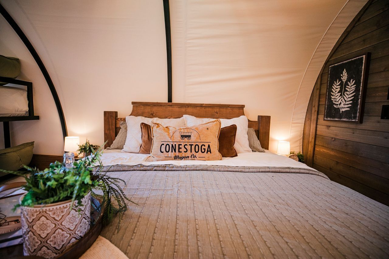 A cozy bedroom inside a tent featuring a bed with a wooden headboard, decorative pillows, and warm ambient lighting.