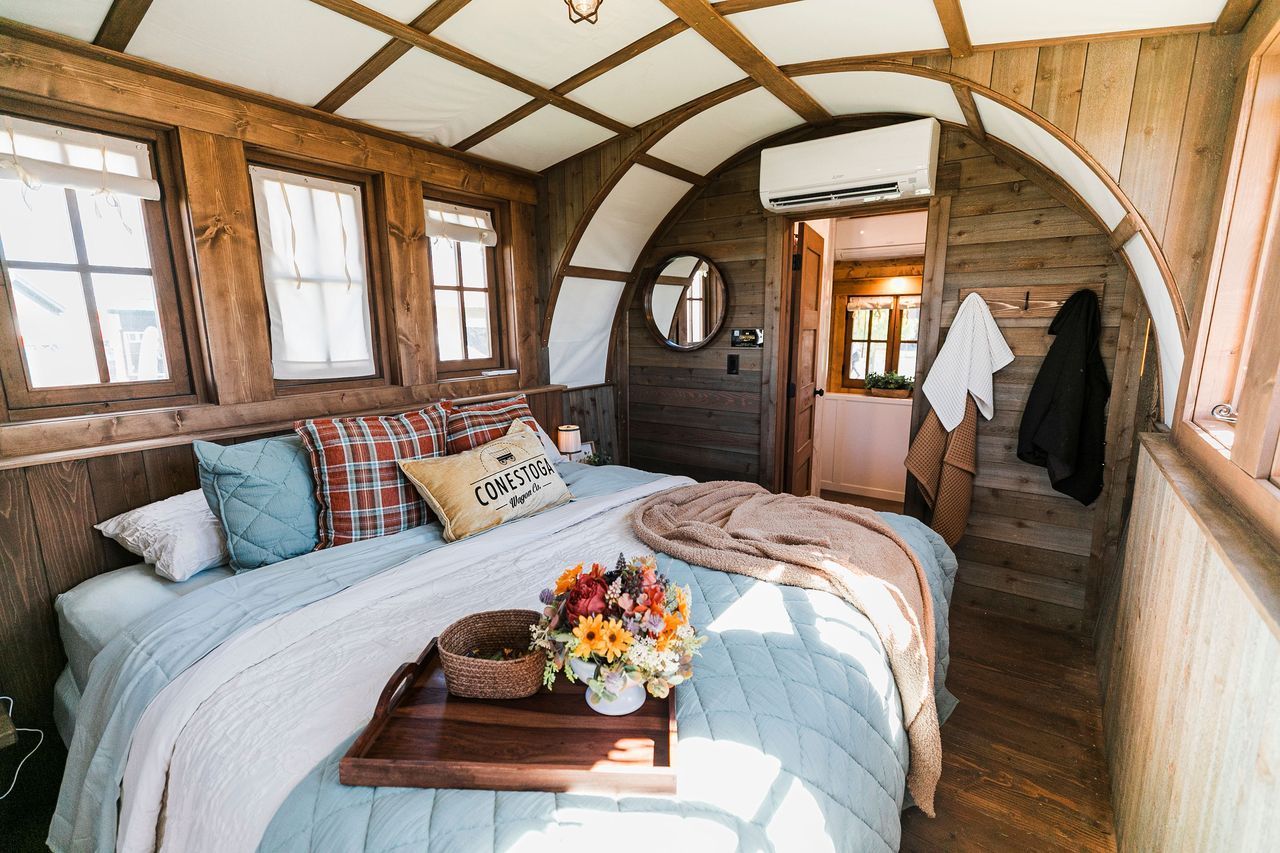 A cozy bedroom in a wooden cabin-style structure with a bed, light blue bedding, and large windows.