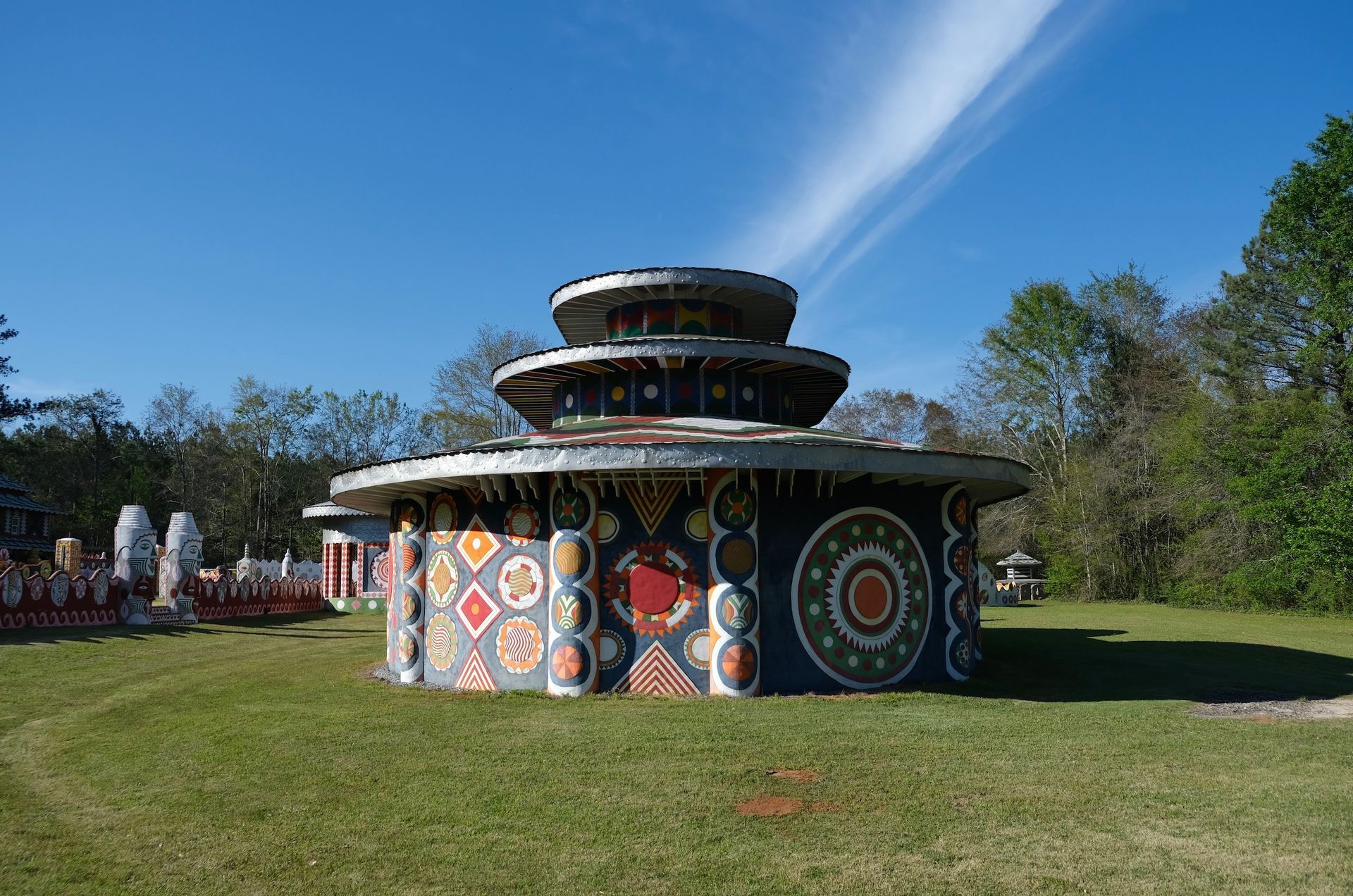 A circular, multi-tiered building with patterned, colorful geometric murals, set in a grassy field under a sunny sky.