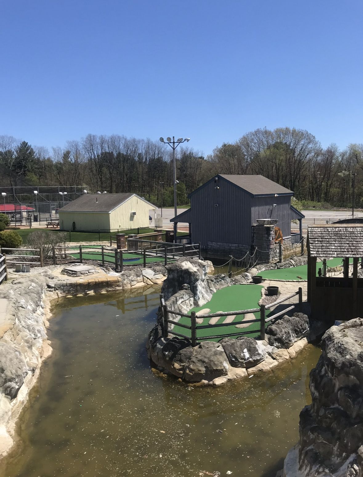 Miniature golf course with water features and buildings under a blue sky.