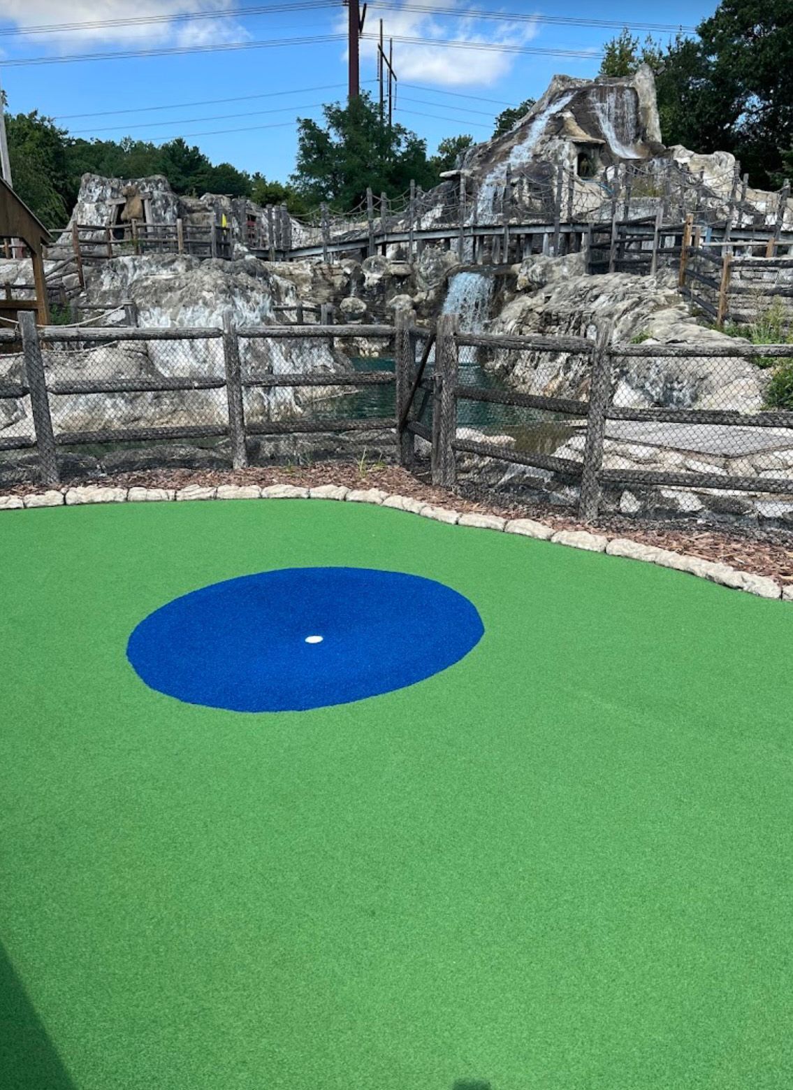 Mini golf green with a blue circle, rock waterfall in background.