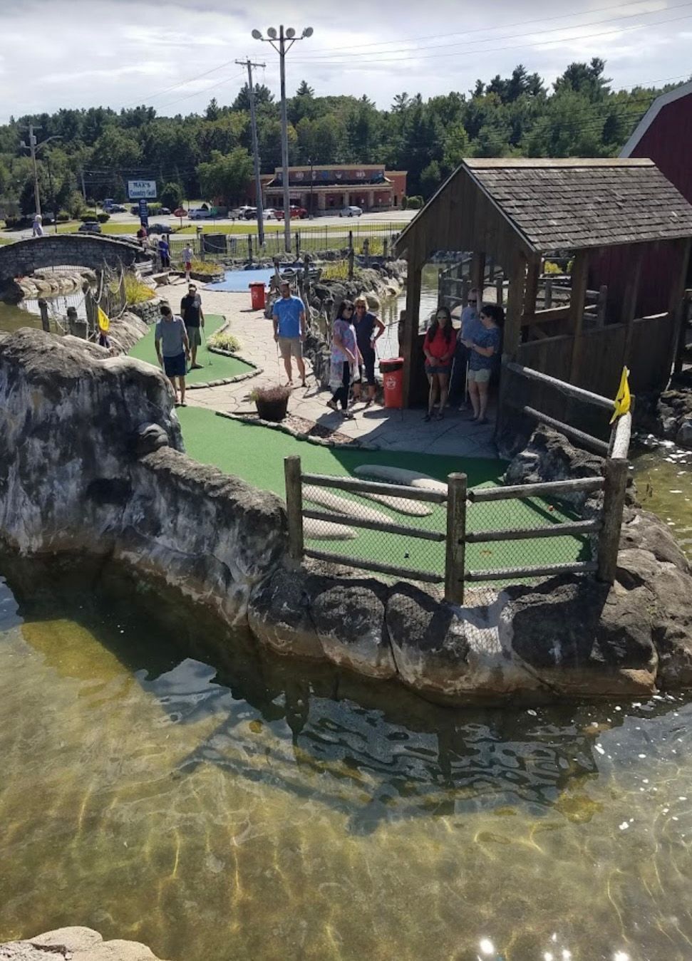 People playing miniature golf on a course with water features and a wooden shack.