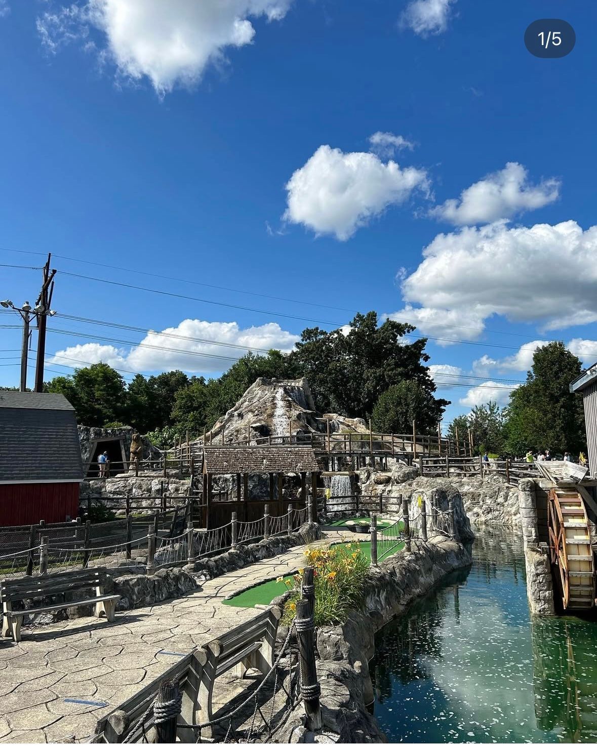 Miniature golf course with stone structures, water feature, and a blue sky.