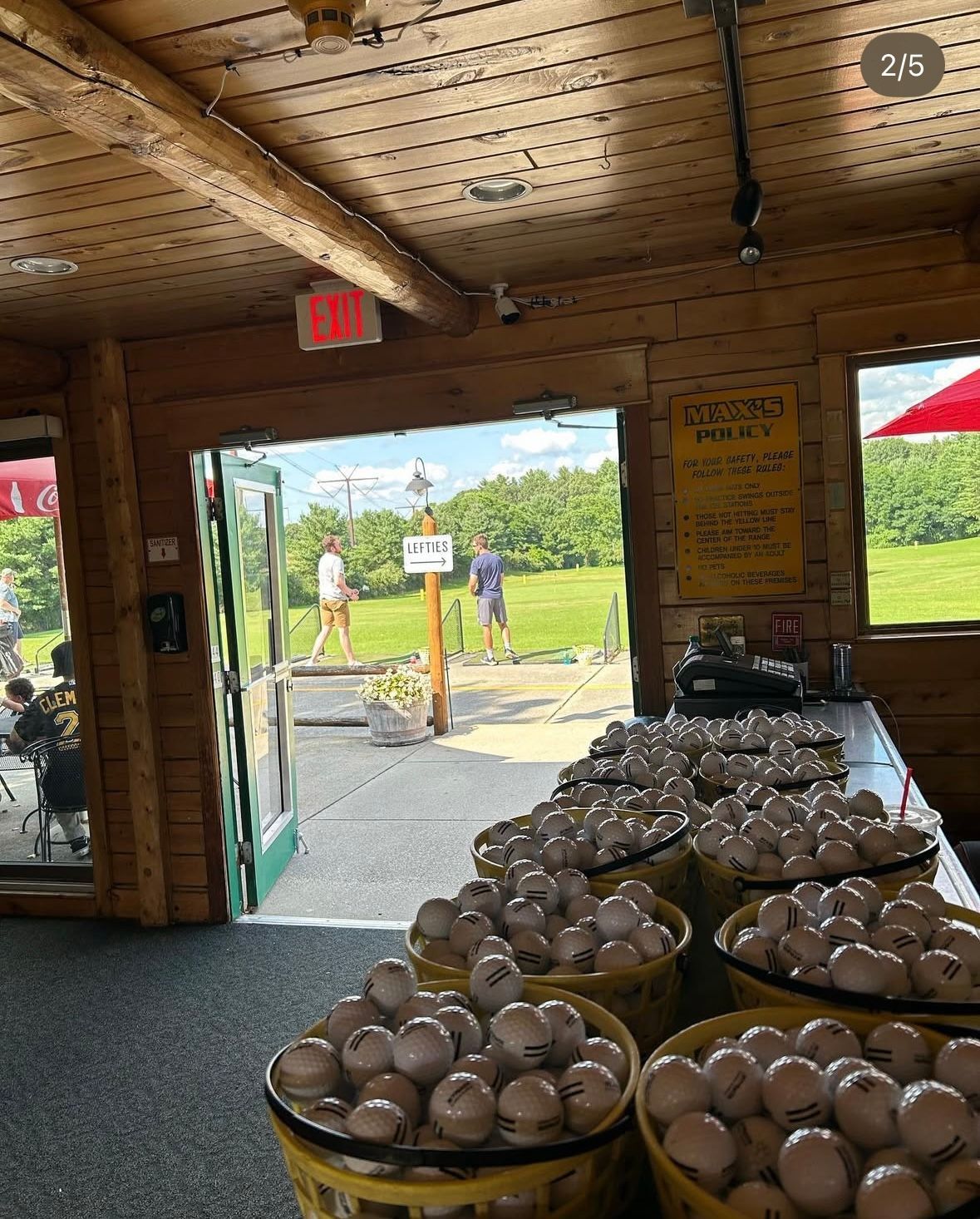 Balls in baskets in a driving range shop, with golfers visible outside.