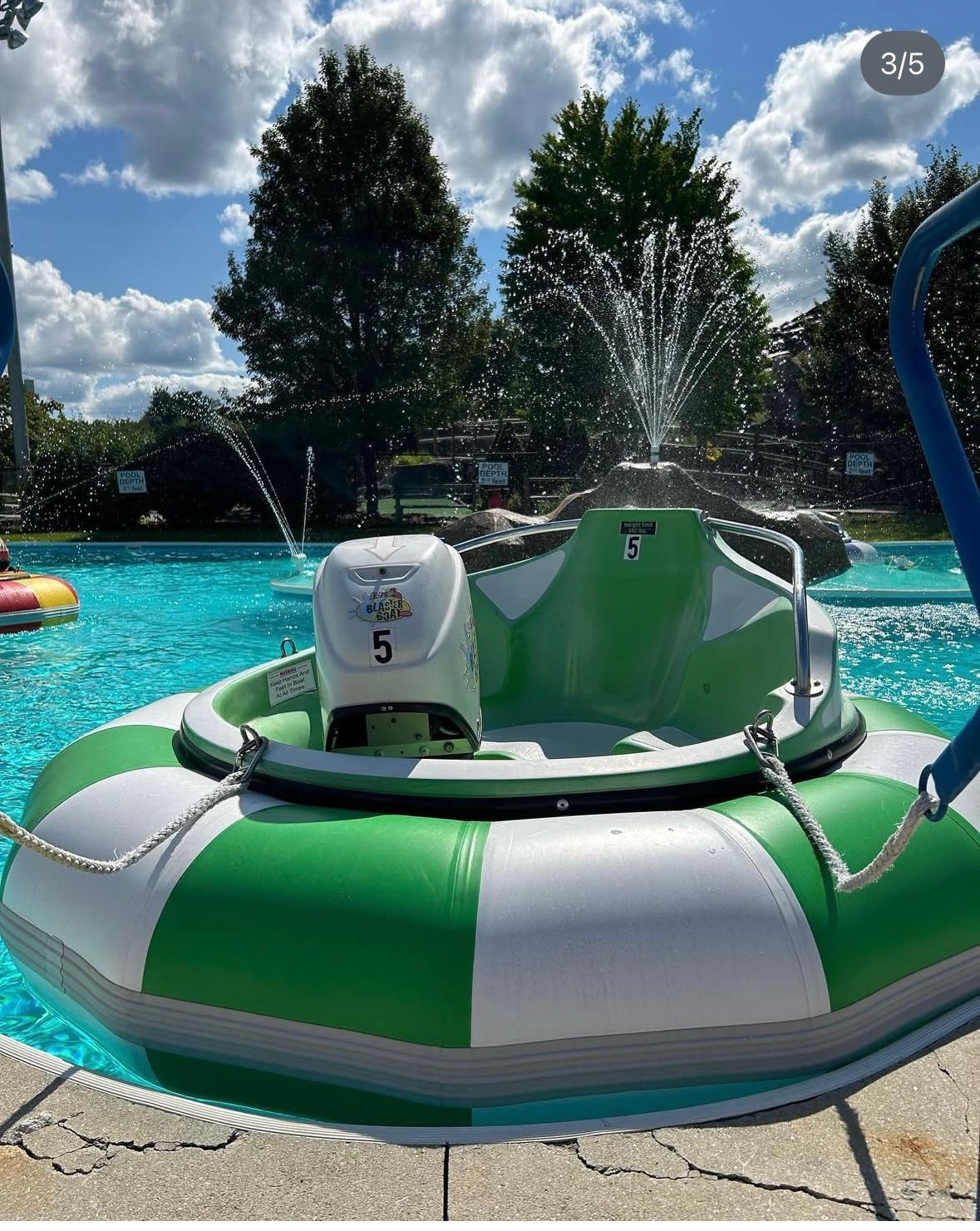 Green and white bumper boat in a pool with a fountain spraying water.
