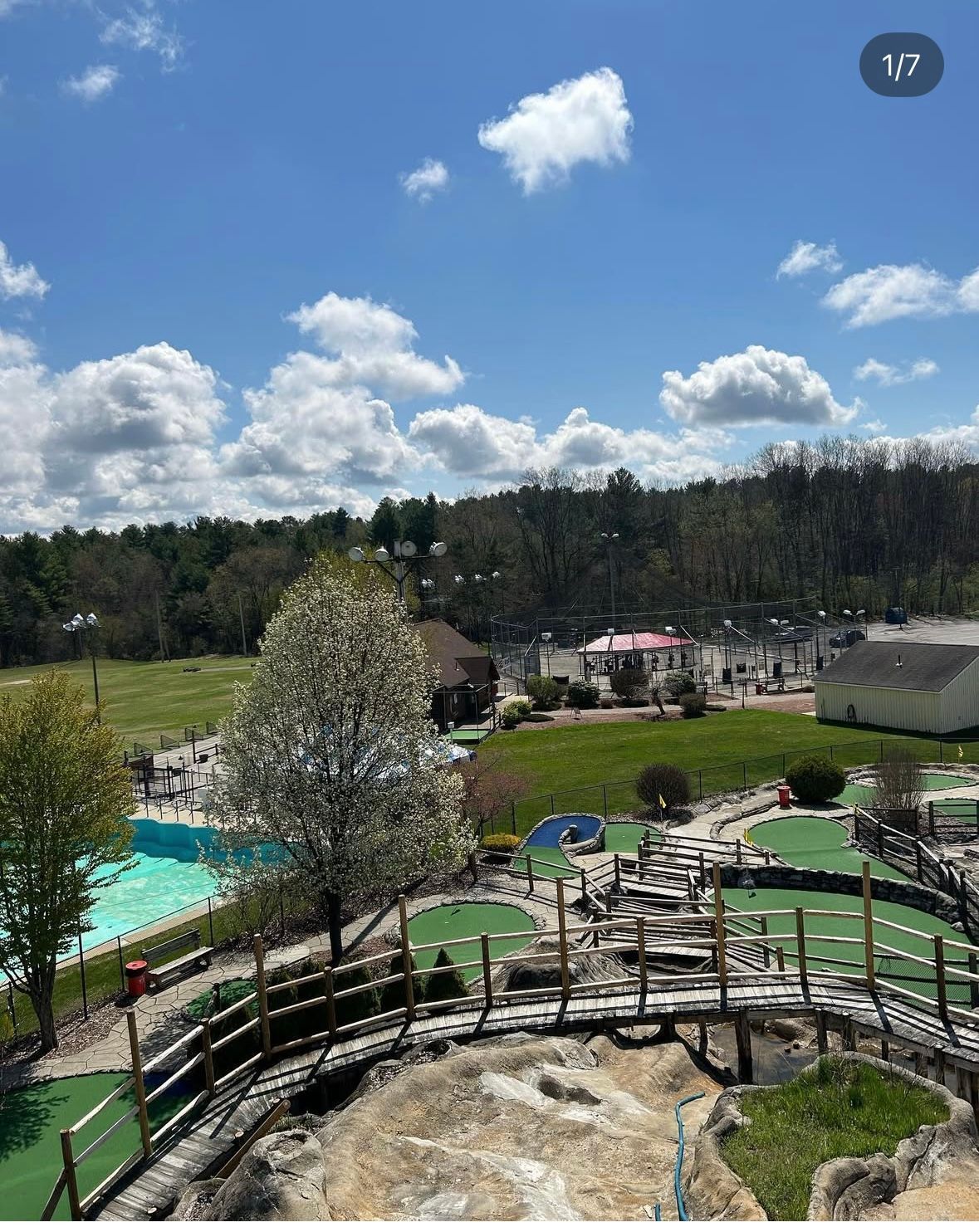Mini golf course with pool, trees, sunny blue sky with fluffy clouds.