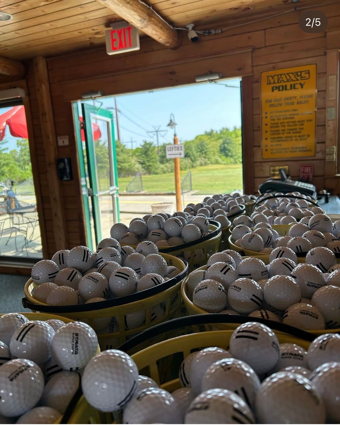 Baskets overflowing with golf balls sit inside a wooden building with an open doorway to a mini golf course.