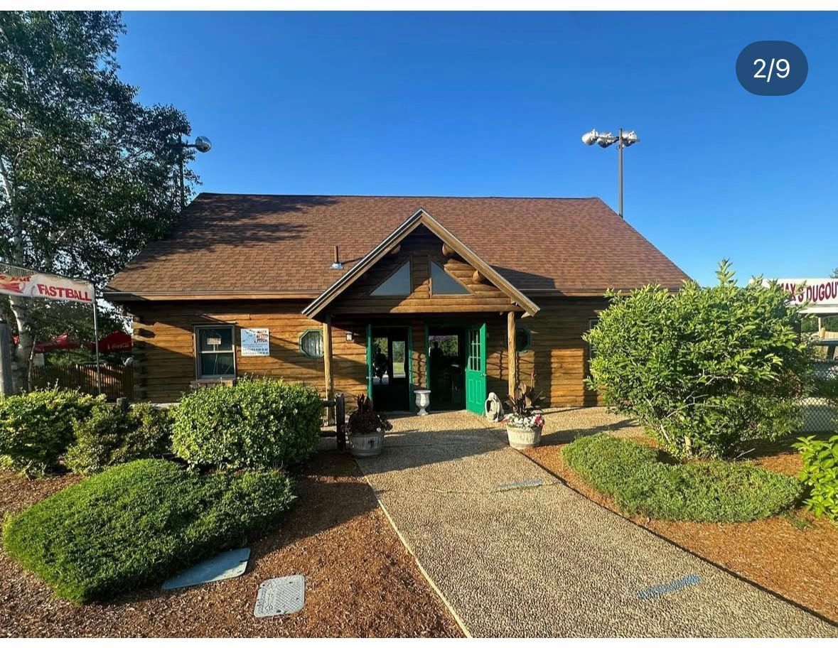 Wooden building with brown roof, green door, and walkway. Bushes and clear blue sky.