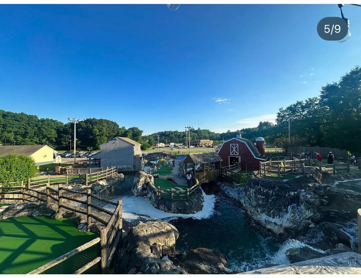 Miniature golf course with a rustic farm theme, water features, and a clear blue sky.