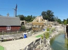 Miniature golf course with wooden structures, water features, and a clear blue sky.