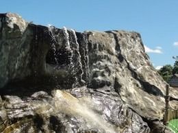 Artificial rock waterfall, water cascading down, blue sky background.