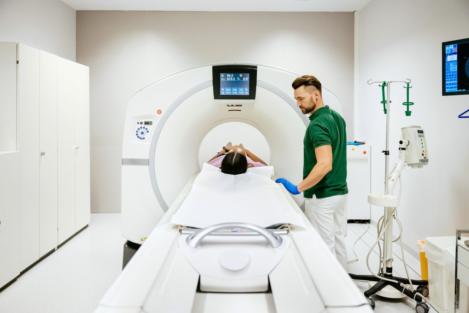 A man is standing next to a woman in a hospital bed getting a ct scan.