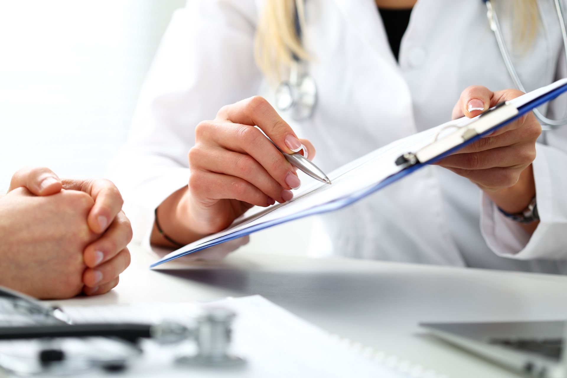 A doctor is holding a clipboard and talking to a patient.