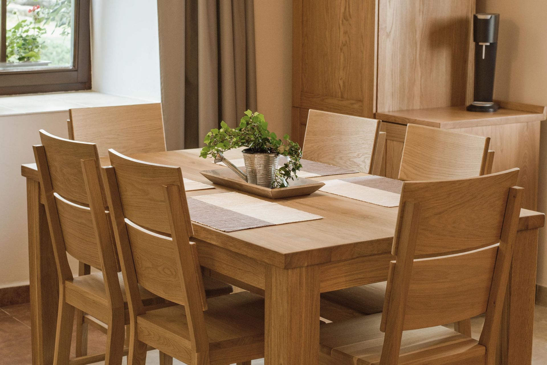 Wooden dining table with six chairs, potted plant, and cabinet.