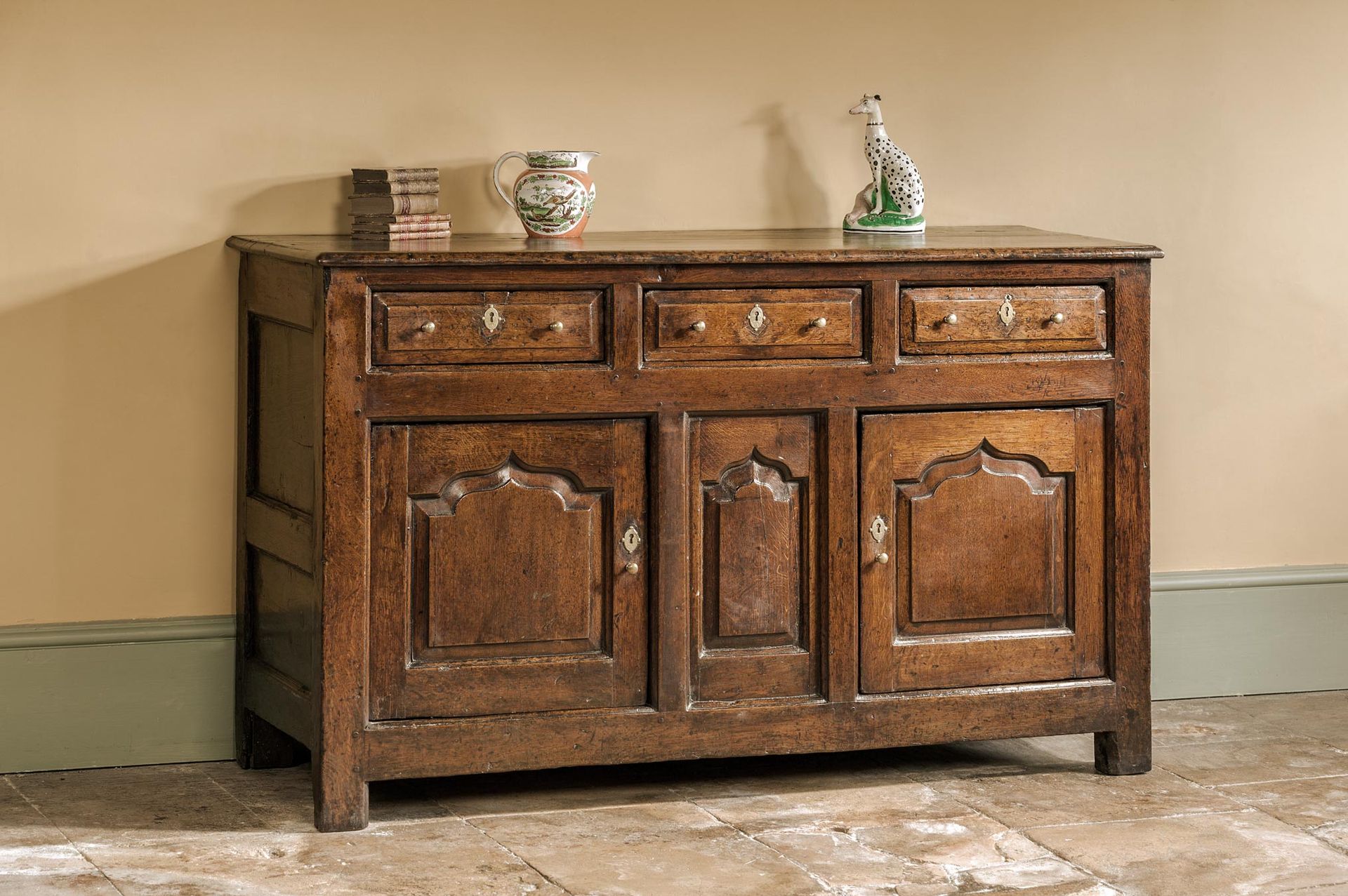 Wooden antique cabinet with three drawers and two doors, items on top.