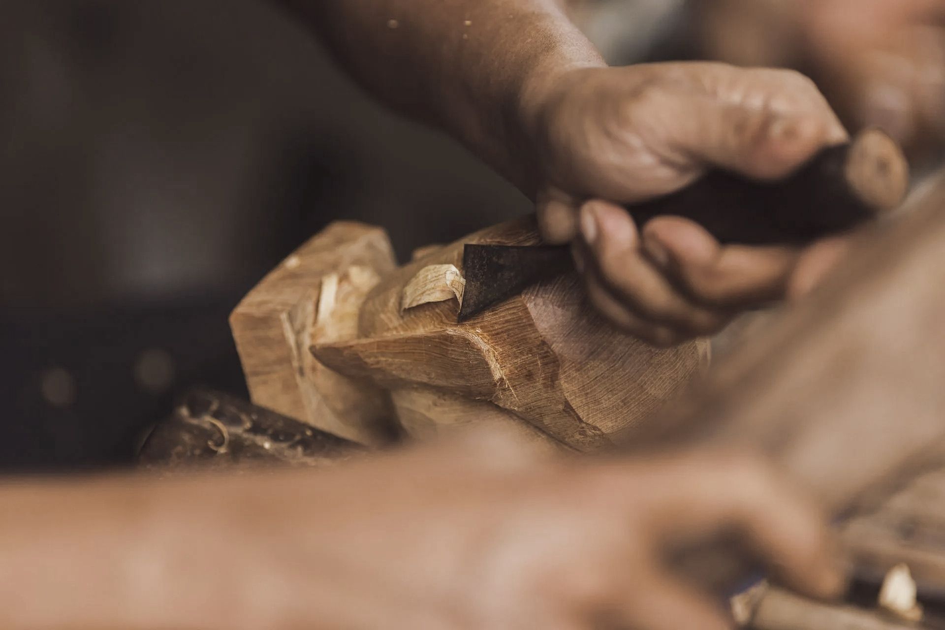 Hands carving wood with a chisel, close-up, working on a wooden piece.