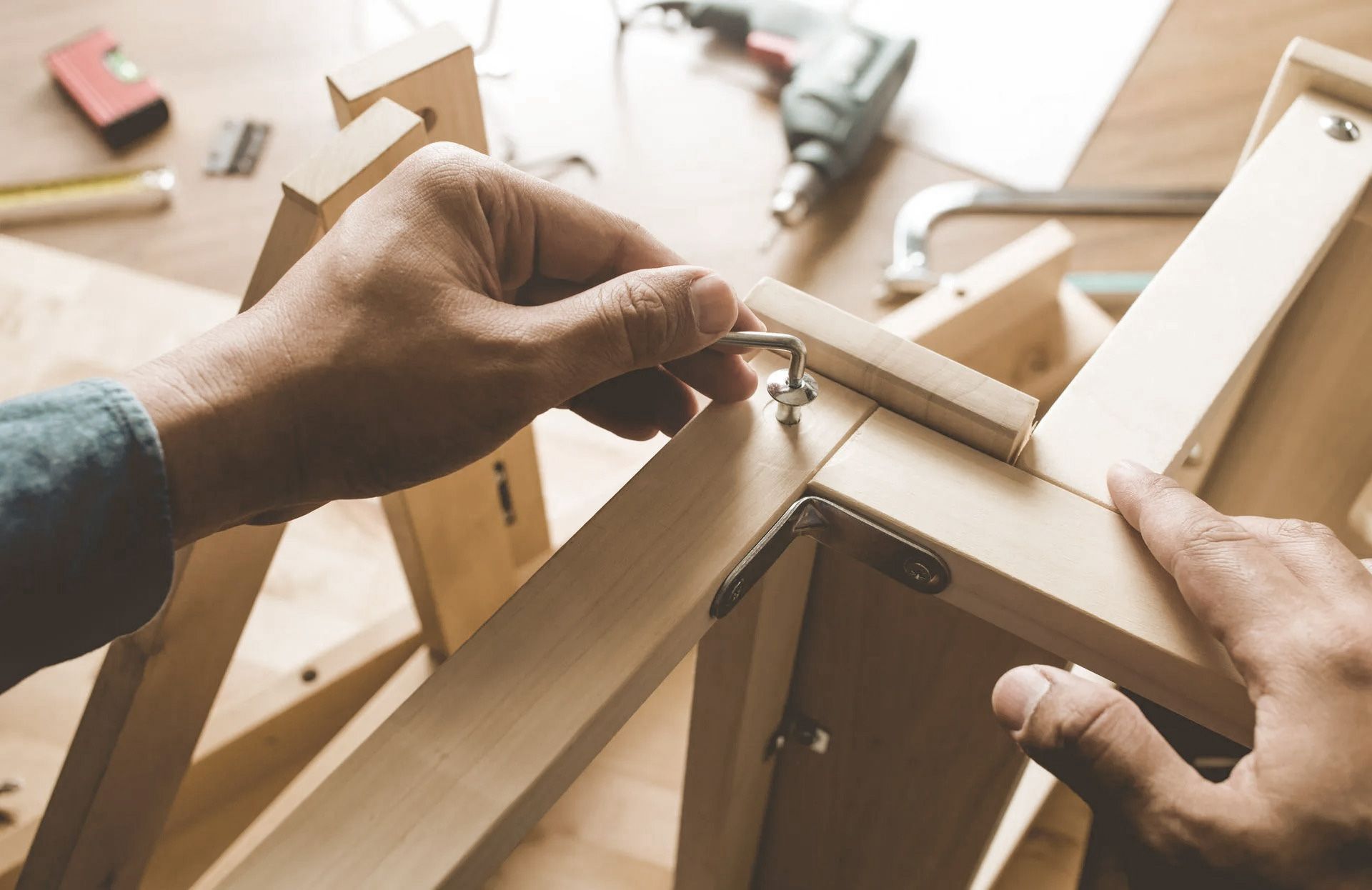Person assembling wooden furniture with a hand tool. Close-up on hands and unfinished wood.