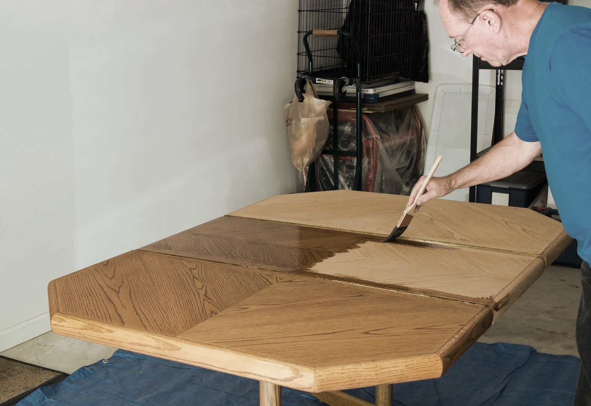 Man applying stain to a wooden table with a brush, in a garage.