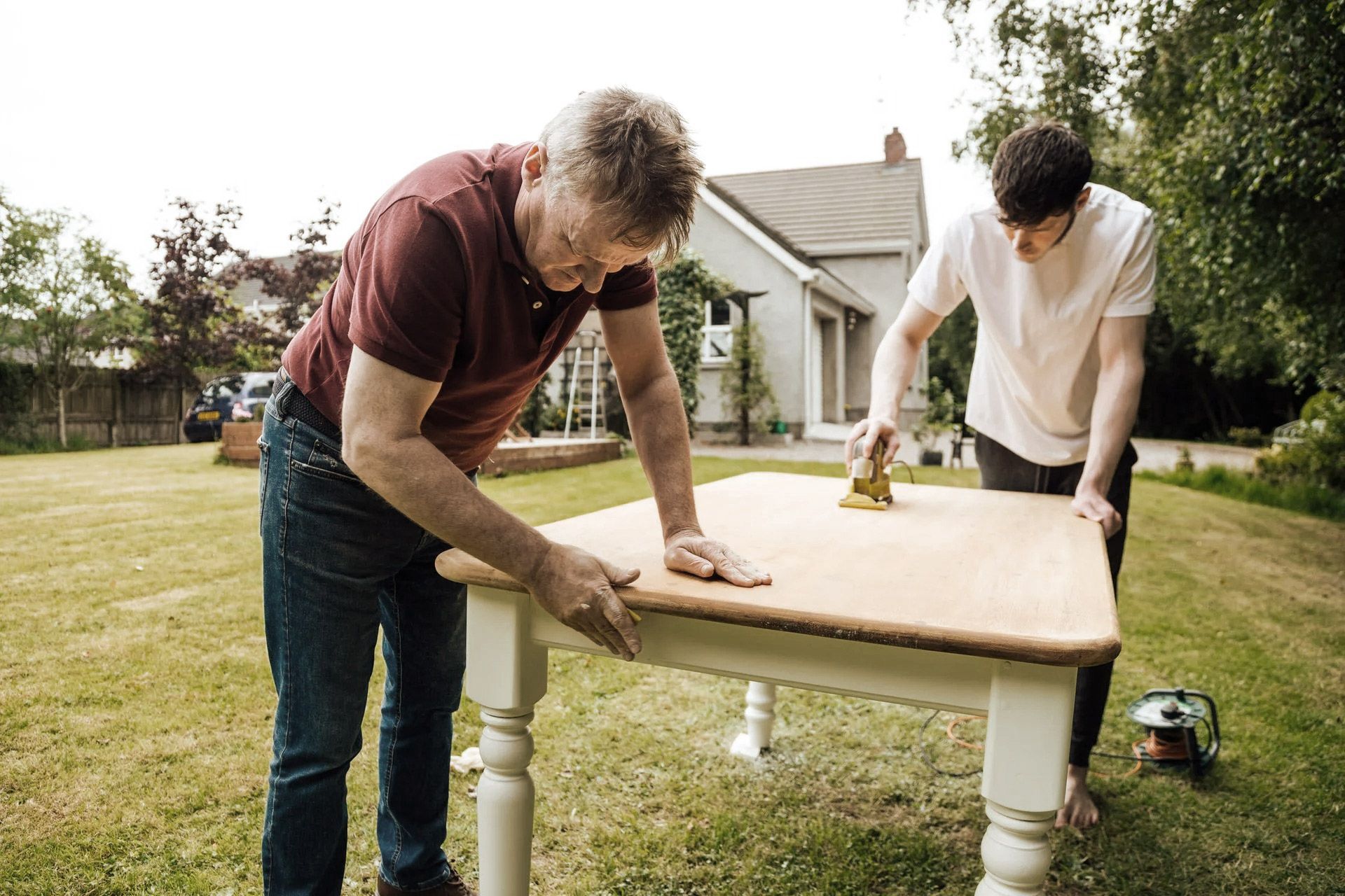 Two people sanding a wooden table outdoors.