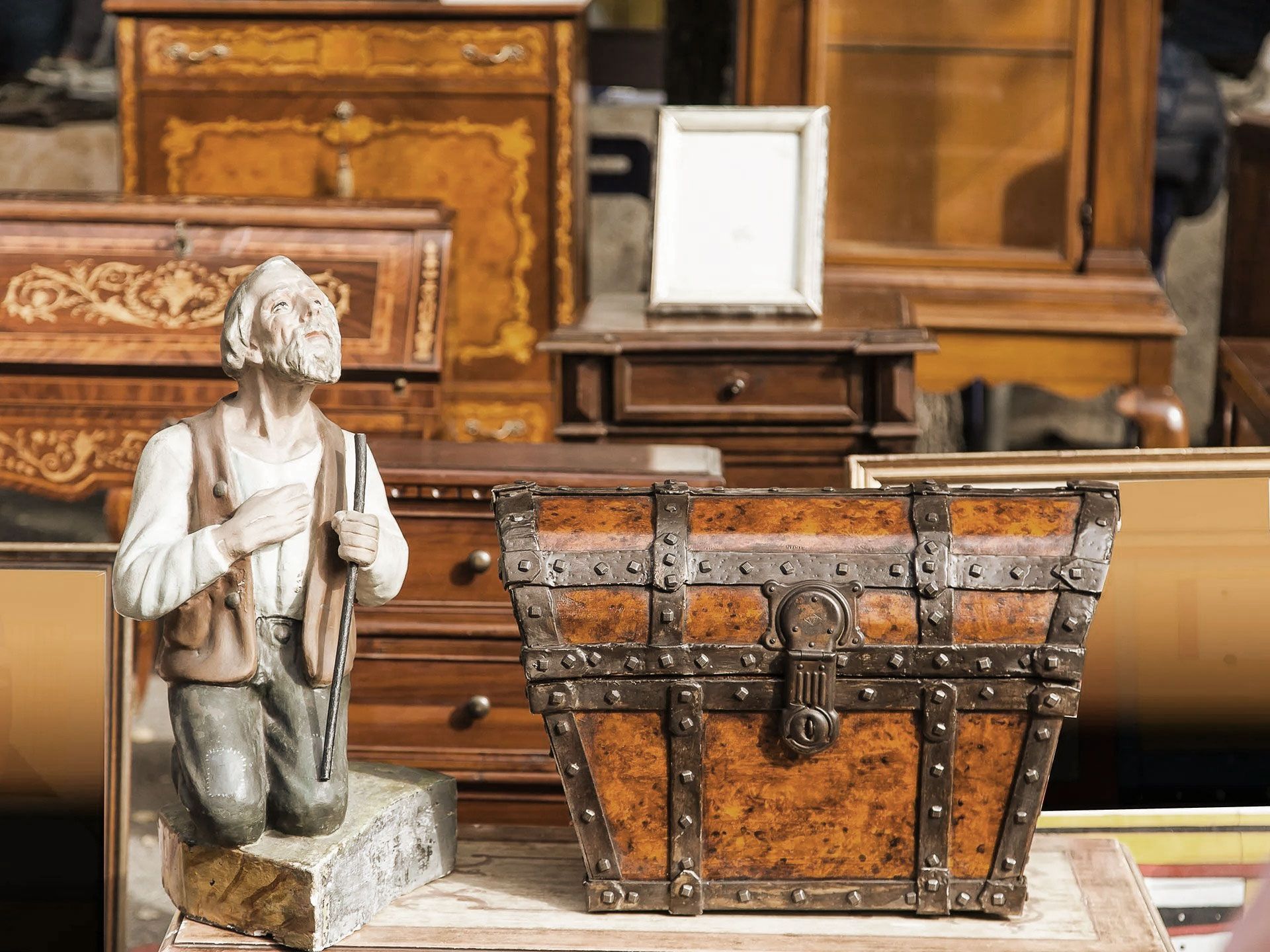 Antique wooden chest with metal hardware and statue in front of other antique furniture.