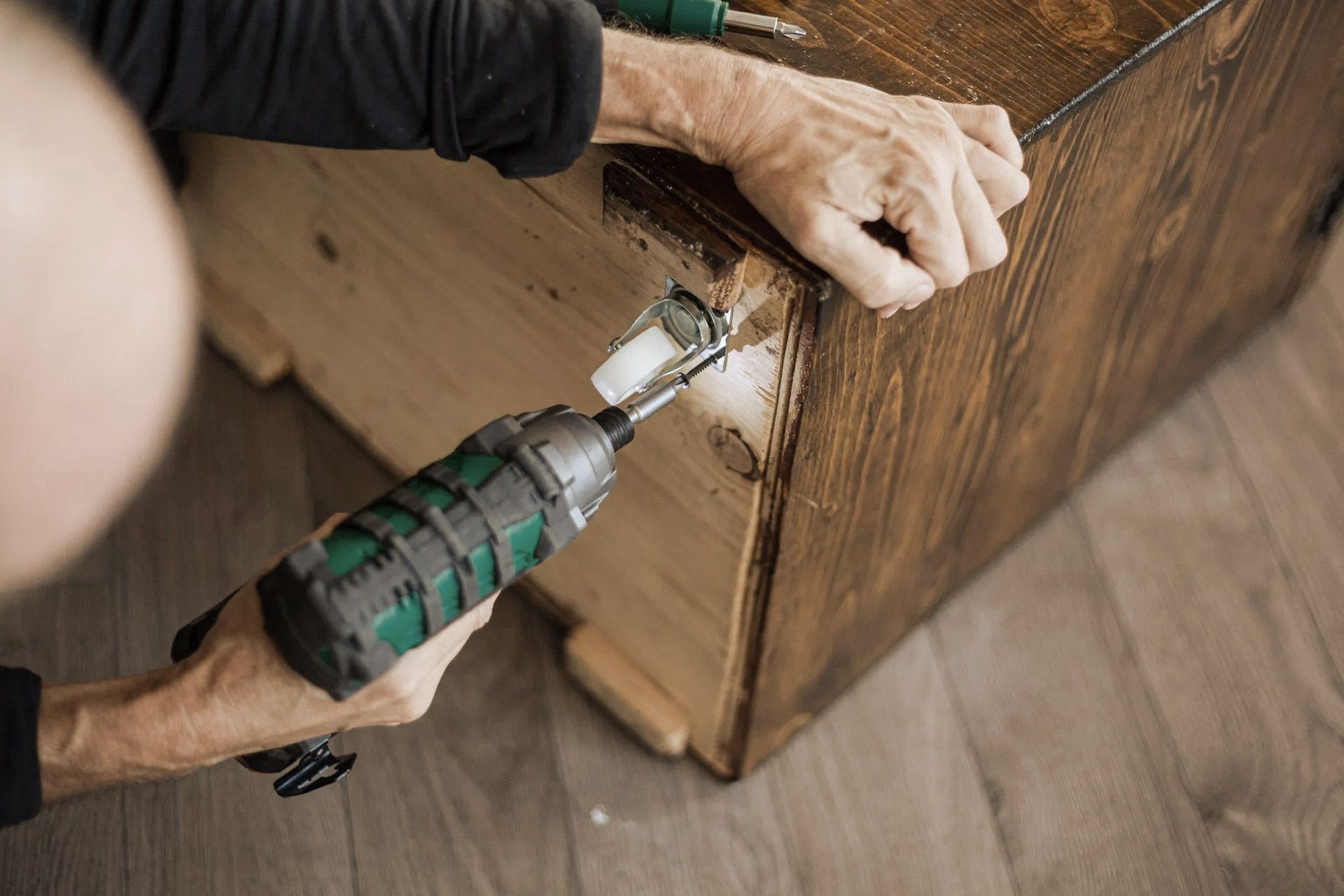 Person using a power drill to assemble or repair a wooden box, indoors.
